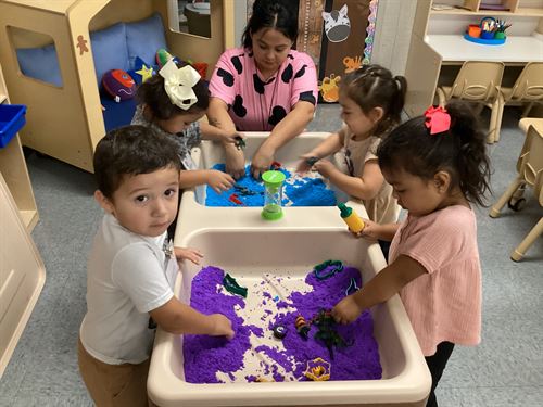Picture of early learners and thier teacher playing with colored sand
